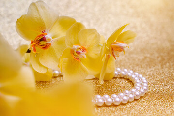 Obraz na płótnie Canvas yellow Orchid and pearl necklace on a shiny gold background 