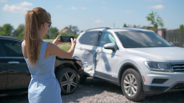 Stressed woman driver taking photo on mobile phone camera after vehicle collision on street side for emergency service after car accident. Road safety and insurance concept