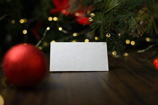 Blank invitation card on wooden table with Christmas ornaments. Blank business card mockup.