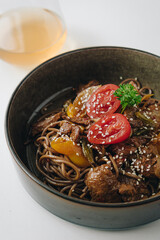 noodles with beef, vegetables, cherry tomatoes and sesame sauce in a deep plate side view