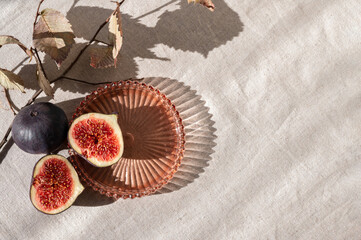 Aesthetic fig fruit autumn composition, cut fig on plate with dried leaves and natural sunlight shadows on neutral beige linen tablecloth. Lifestyle, fall healthy vitamin food, diet concept