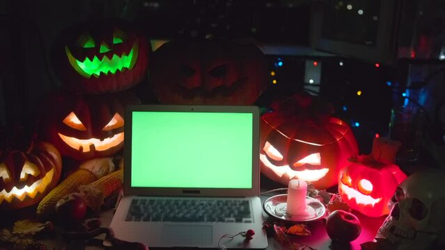 Laptop with chromakey in dark and many glow jack o'lanterns, candles, pumpkins, holiday background. Mysterious atmosphere Happy Halloween night party goosebumps.