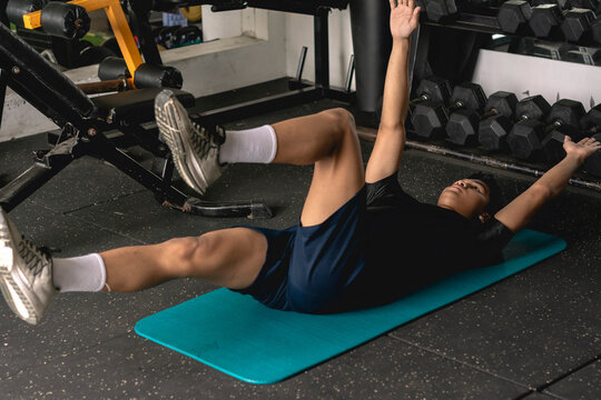 A young man doing a set of dead bug exercises lying on a mat. Leg and arm raised alternately. Abdominal and core workout at the gym.