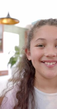 Vertical video of half face of happy biracial girl with long, curly hair smiling in sunny kitchen