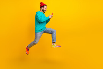 Fototapeta na wymiar Full length photo of cheerful man wear turquoise pullover running to empty space look at smartphone isolated on yellow color background