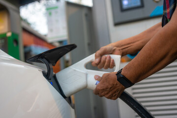 Asian mature woman hold charging cable to electric car at station