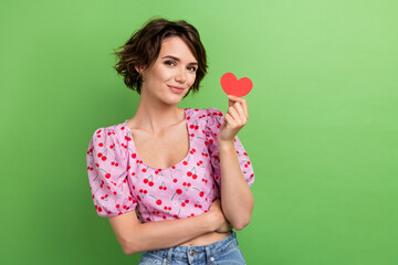 Photo of cute good mood woman with bob hairstyle dressed pink blouse hand holding paper red heart isolated on green color background
