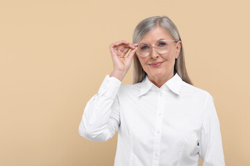Portrait of beautiful senior woman in glasses on beige background. Space for text
