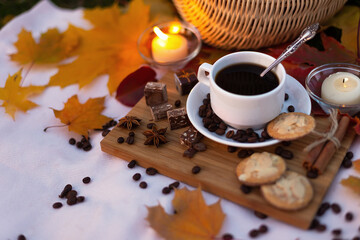 Evening picnic by candlelight with coffee, cookies and chocolate in autumn park with maple leaves. Still life. Food outdoors