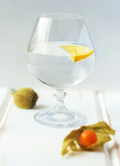 Glass of water with lemon on wooden table with ripe physalis. Still life
