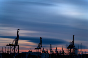 Fototapeta na wymiar Sunset Over Busy Commercial Port with Silhouette of Massive Cranes