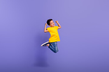 Fototapeta na wymiar Full body photo of charming young boy jumping summer vacation raise hands dressed yellow outfit isolated on violet color background