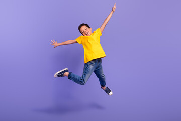 Fototapeta na wymiar Full size photo of cute young schoolboy jumping have fun playing dressed yellow clothes isolated on violet color background