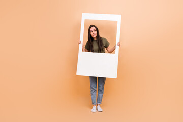 Full length photo of impressed funky lady wear khaki t-shirt looking photo frame isolated beige color background