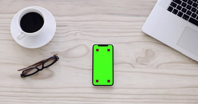 Phone, green screen and office desk background for marketing or social media mockup on table top. Mobile app, coffee cup and space for contact information, chat and tracking markers in moving effect