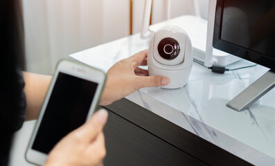 Female hands holding smart phone and installing wireless CCTV camera at house for security.