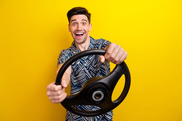 Portrait of astonished positive man arms hold steering wheel open mouth isolated on yellow color...