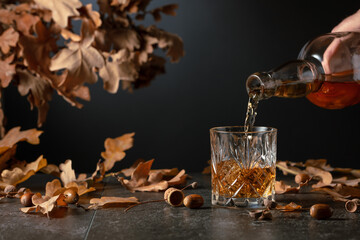 Whiskey on a black table with dried-up oak leaves.