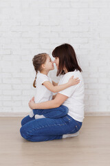 Happy mother and daughter sitting on the floor in jeans and white t-shirts