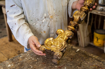 Artigiano restauro, mostra in primo piano candelabro da restaurare. Dorato, doratura, d'antiquariato.