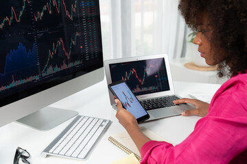 African woman blogger with serious face, looking on screen monitor and smartphone with stock market achievement at high profit. Concept of exchange investment online in trading on pc. Tastemaker.