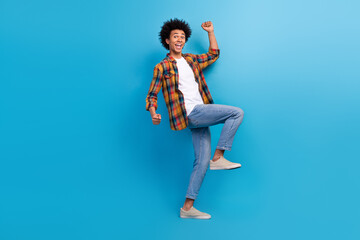 Full length photo of positive lucky guy wear plaid shirt walking rising fists screaming yeas...