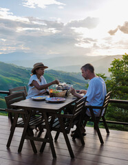 a couple of men and women on vacation in Northern Thailand, staying at a homestay cabin hut in the mountains of Chiang Rai Doi Chang enjoying dinner with a Thai BBQ at sunset in the mountains