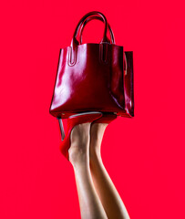 Stylish red female leather bag. Perfect female legs wearing high heels. Shapely legs, a girl in shoes high-heeled. Red glossy female leather bag