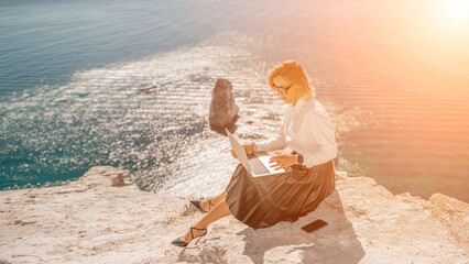 Fototapeta na wymiar Business woman on nature in white shirt and black skirt. She works with an iPad in the open air with a beautiful view of the sea. The concept of remote work.
