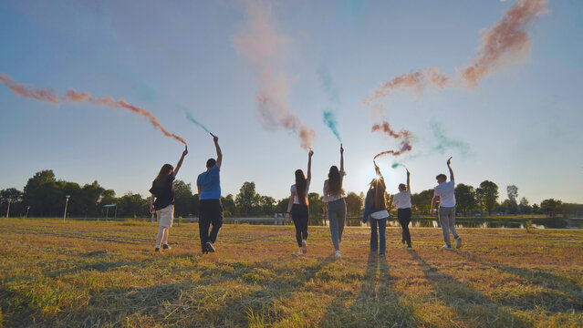 A group of friends spraying multi-colored smoke at sunset. - Powered by Adobe