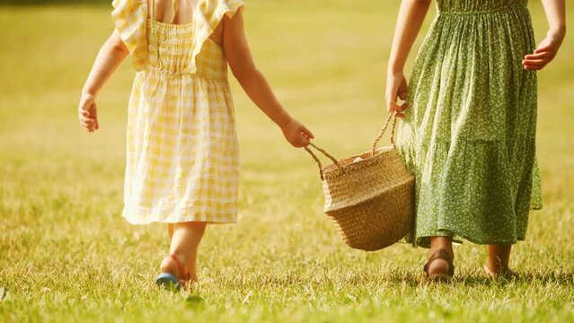 Two little sisters walk with a basket on green grass together on a sunny summer day