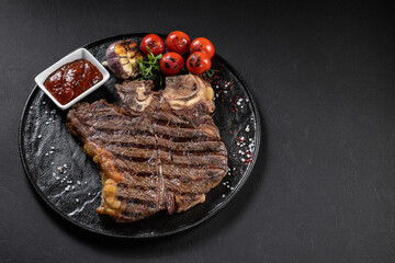 BBQ beef steak with sauce on a black plate with vegetables, tomatoes and corn. Black background. Restaurant supply.