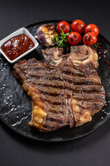 BBQ beef steak with sauce on a black plate with vegetables, tomatoes and corn. Black background. Restaurant supply.