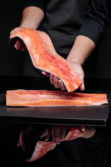 A cook on a black background cuts a whole salmon carcass.