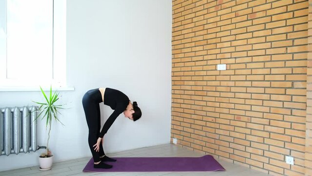 Beautiful sporty girl practices yoga, pilates at home doing downward-facing dog pose. Fitness training. Healthy body. Hatha practicing. Slim 30s woman in black clothing. Adho Mukha Svanasana