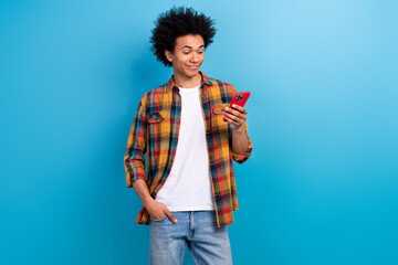 Portrait of intelligent guy with afro hairstyle wear checkered shirt look at smartphone read email isolated on blue color background