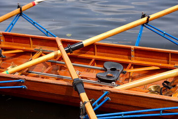 Ein Ruderboot, Mehrsitzer hat an einem Steg an einem Boothaus fest gemacht.
