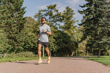 A sporty young man running alone. Daily training development of the cardiac system. Uses a fitness watch on his arm. Slim body and active lifestyle.