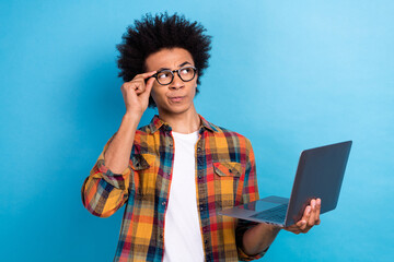 Portrait of thoughtful minded guy with afro hairstyle touch glasses hold laptop look empty space isolated on blue color background