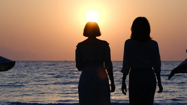 silhouette of two women walking on the beach at sunset