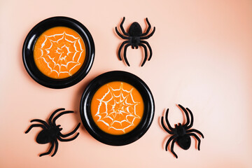 Pumpkin cream soup with spider web of fresh cream in a black bowl with spider decorations. Halloween food concept.