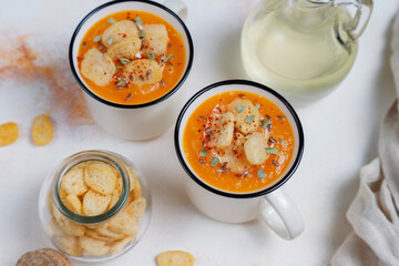 Roasted butternut squash soup with cream and pumpkin seeds on two white mugs.