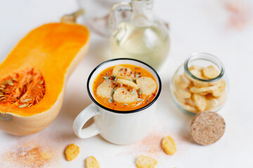 Roasted butternut squash soup with cream and pumpkin seeds on two white mugs.