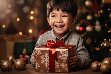 Fototapeta na wymiar A little Asian boy holds a Christmas present in his hands with sincere joy and a smile. Christmas and New Year time