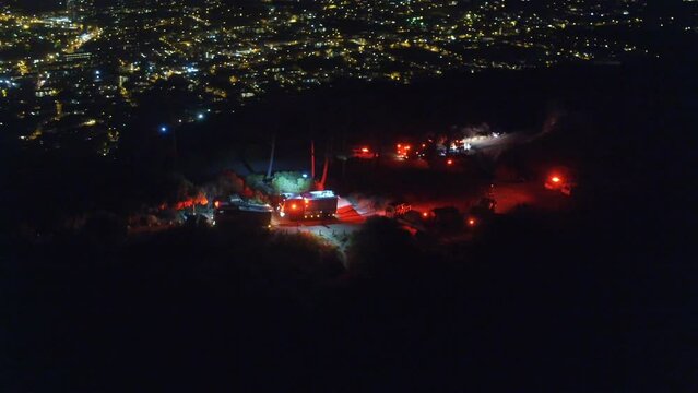 Emergency vehicle, forest fire and service at night in drone aerial view for danger, safety and city protection. Firefighter truck, red lights and mountains for natural disaster in cityscape and dark