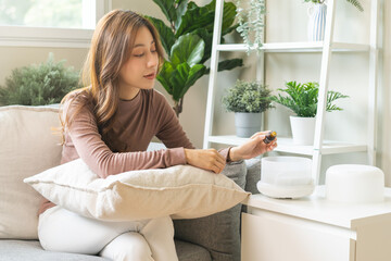 Happy asian young woman, girl hand holding bottle of essential and drop oil into air humidifier, enjoy aromatherapy steam scent diffuser comfortable while rest in living room, apartment at home.