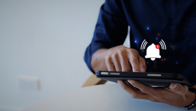 Concept of Remote online alerts on the Application. A businessman's hand holds the iPad and presses the button of Notification bell button on the iPad, unread message, or email notification. 