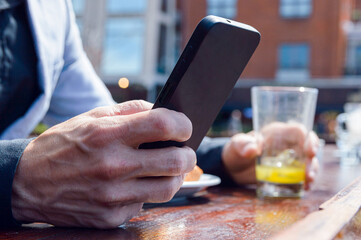 closeup of man sitting at outdoor restaurant, holding phone with one hand while having breakfast