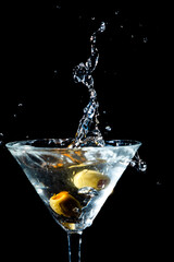 Olive splashing into a martini glass
