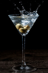 Olive splashing into a martini glass
